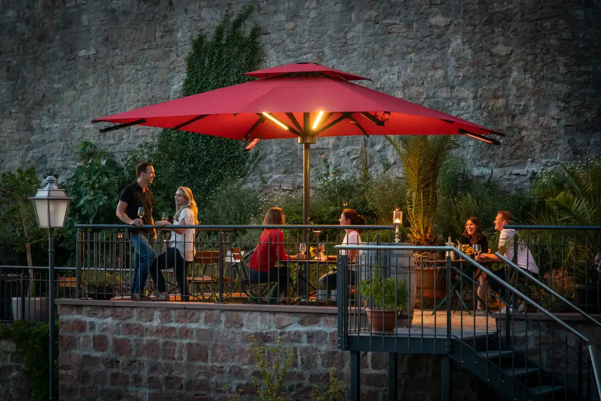 Gemütliche Abendstimmung in einem Außenbereich mit rotem Sonnenschirm und Menschen bei einem Drink