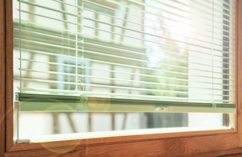 Elegantes Holzfenster mit Alu-Jalousien und Fachwerkhaus gegenüber