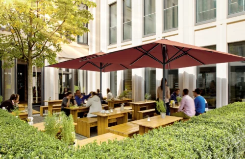 Außenbereich eines Cafés mit Holzbänken und rotem Sonnenschirm